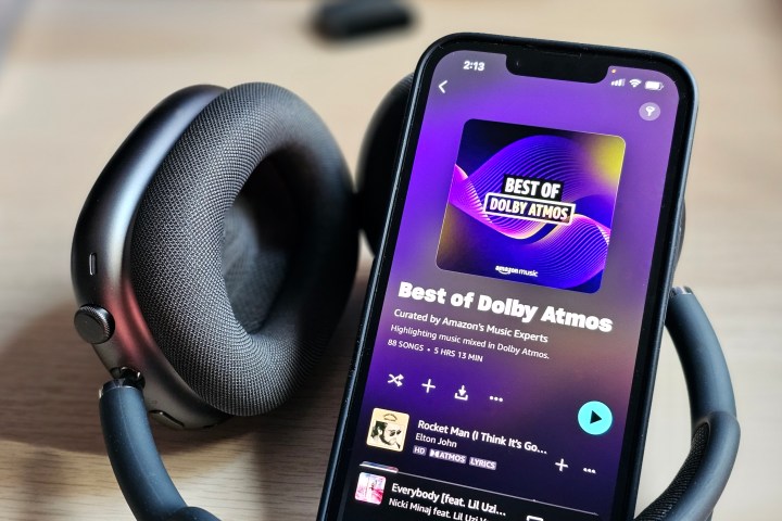 iPhone 14 يعرض تطبيق Amazon Music مع قائمة تشغيل Dolby Atmos Music، بجوار مجموعة سماعات Apple AirPods Max.