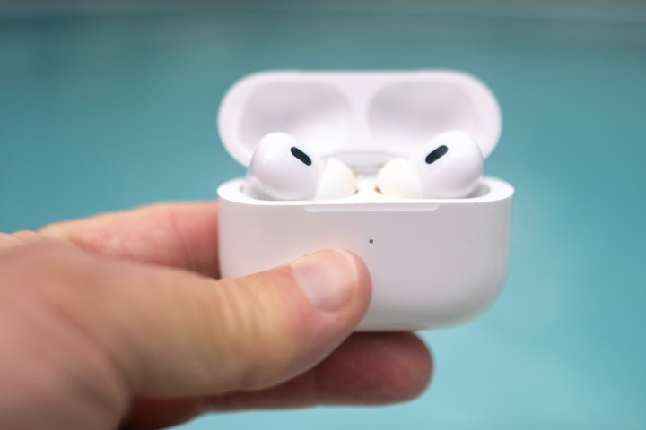 زوج من سماعات Apple AirPods Pro في علبة مفتوحة مع حوض سباحة في الخلفية.