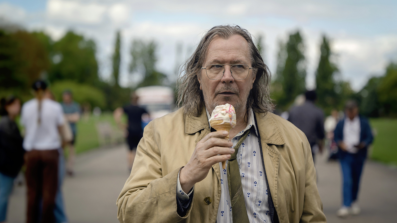 غاري أولدمان في Slow Horses Season 3 على Apple TV+، وهو يسير في الشارع يأكل الآيس كريم.