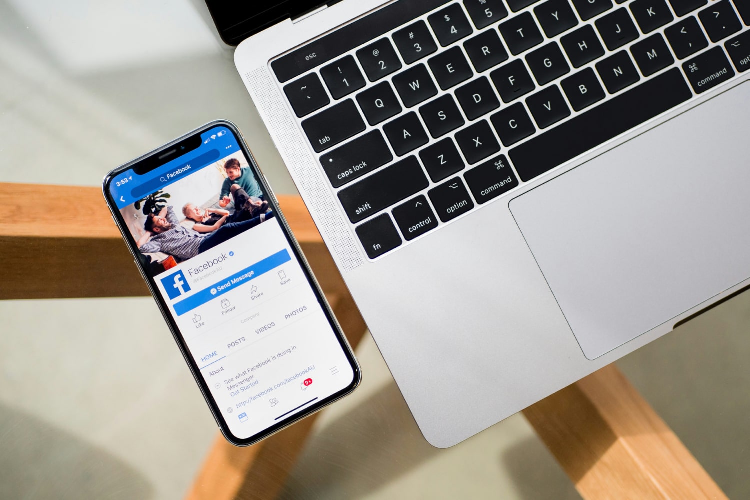 iPhone بجوار جهاز MacBook. يعرض iPhone تطبيق Facebook.