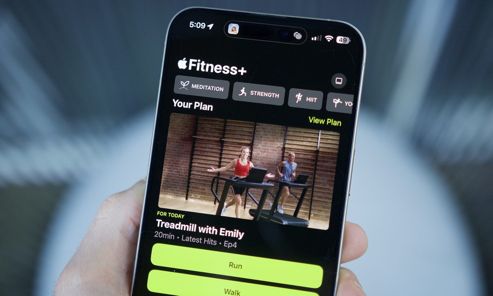 شخص يحمل جهاز iPhone مع فتح تطبيق Apple Litness ، مما يوضح ميزة الخطط المخصصة.