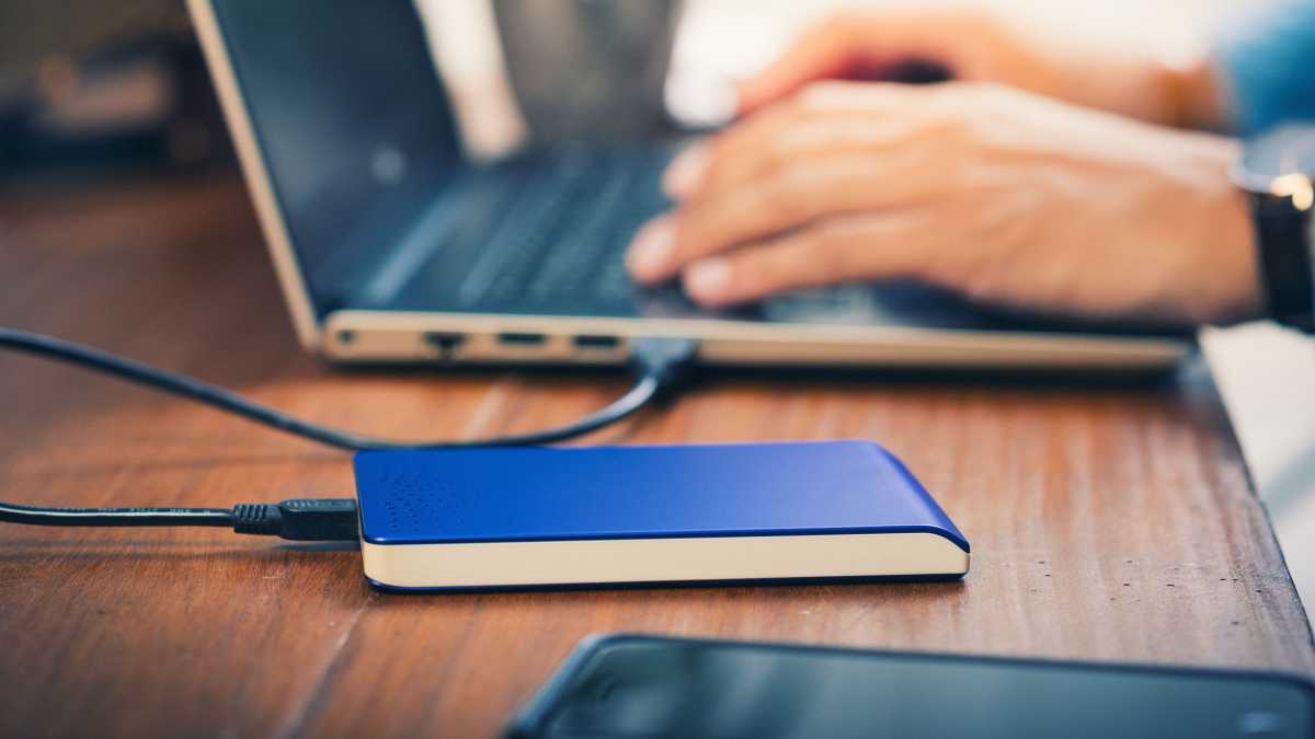 SSD/HDD الخارجي على جدول بجوار دفتر/كمبيوتر محمول ، يكتب رجل على لوحة المفاتيح